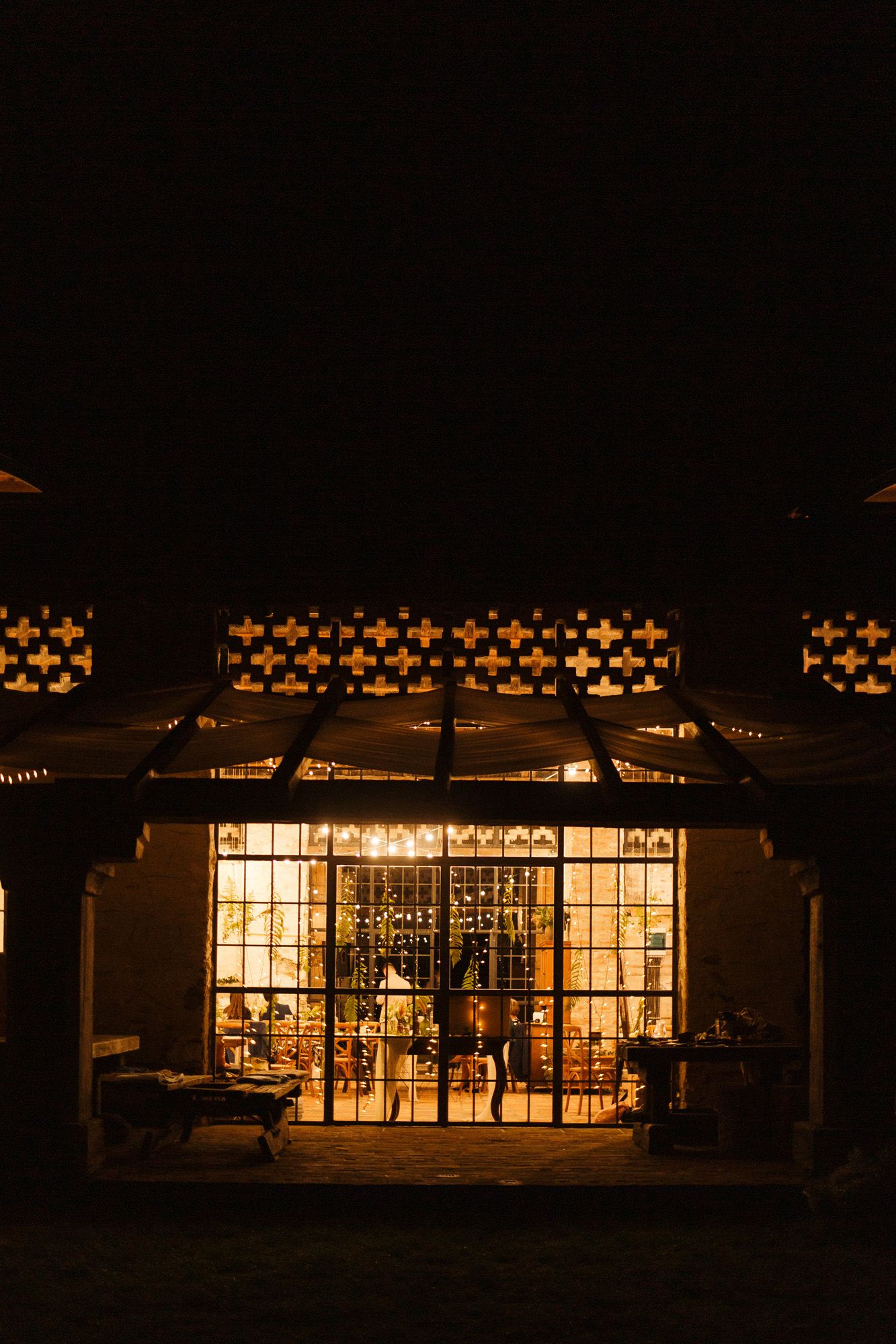 Illuminated glass greenhouse pavilion glowing warmly at night with decorative lights and patterns above.