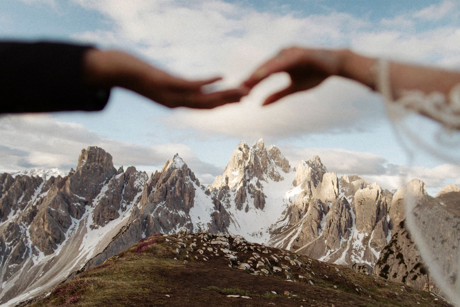 Close-up of hands reaching towards each other with jagged mountain peaks in the background.