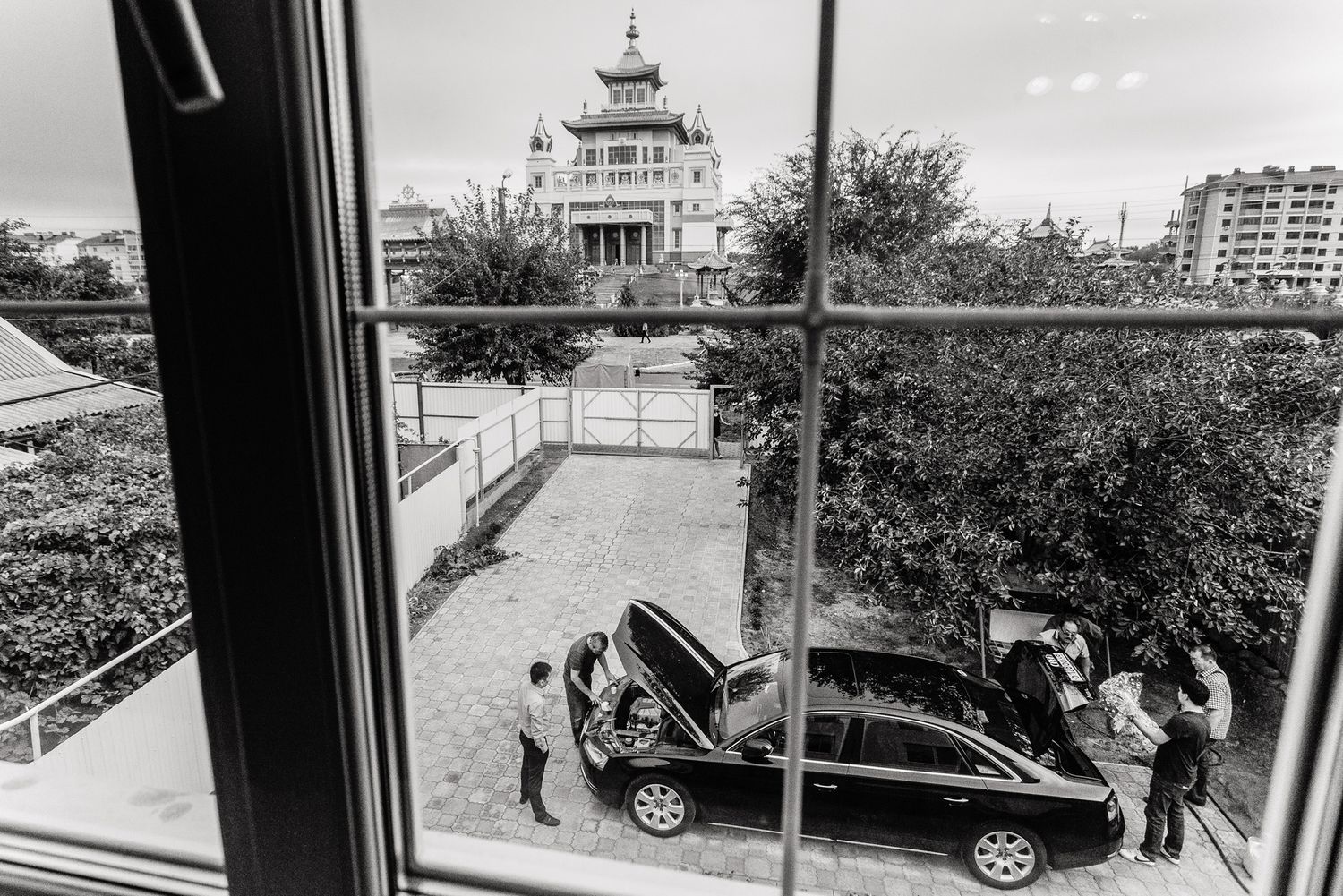 Black and white view of car and people through window with historic building in background.