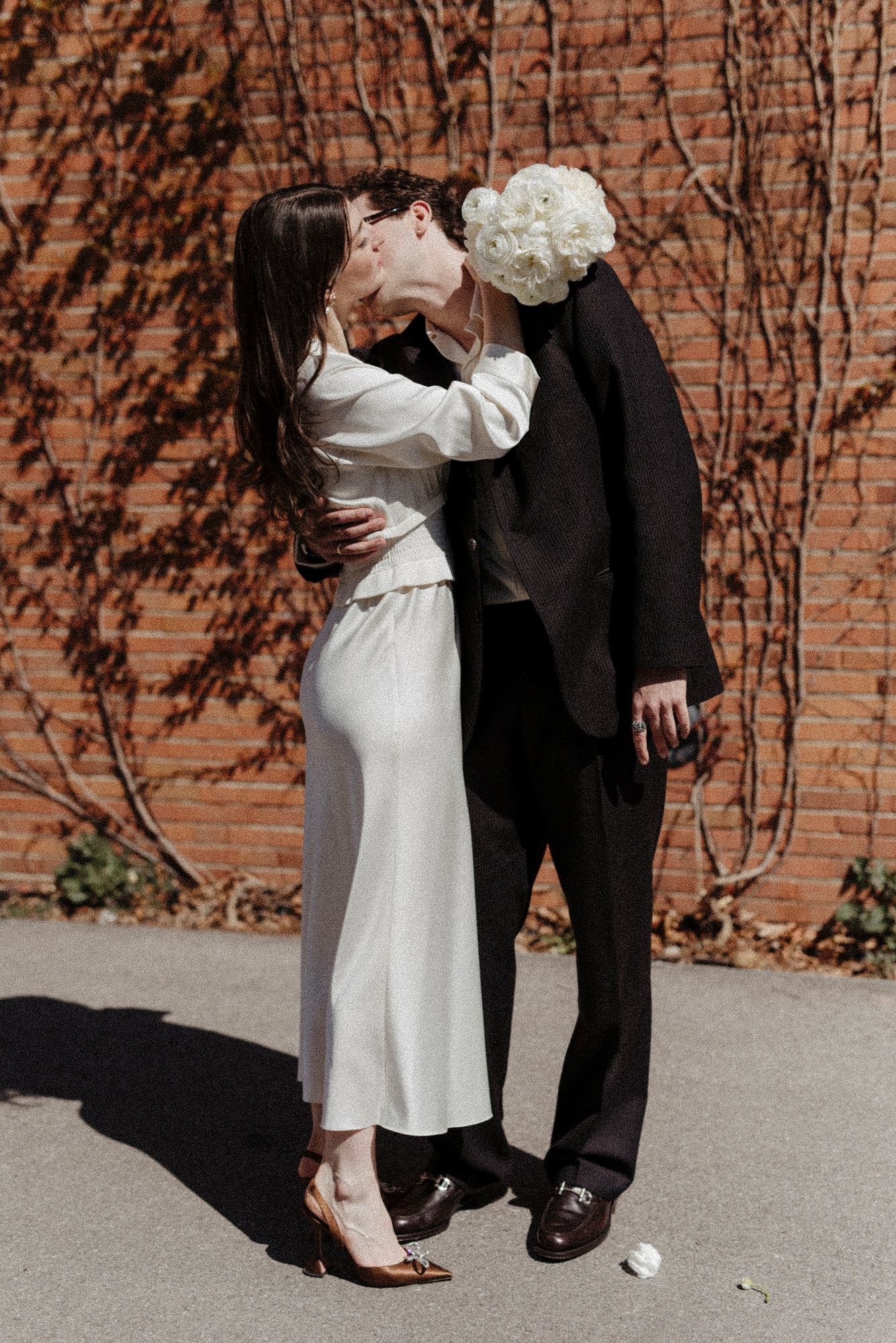 Wedding couple's lower bodies shown against brick wall in contrasting black and white attire.