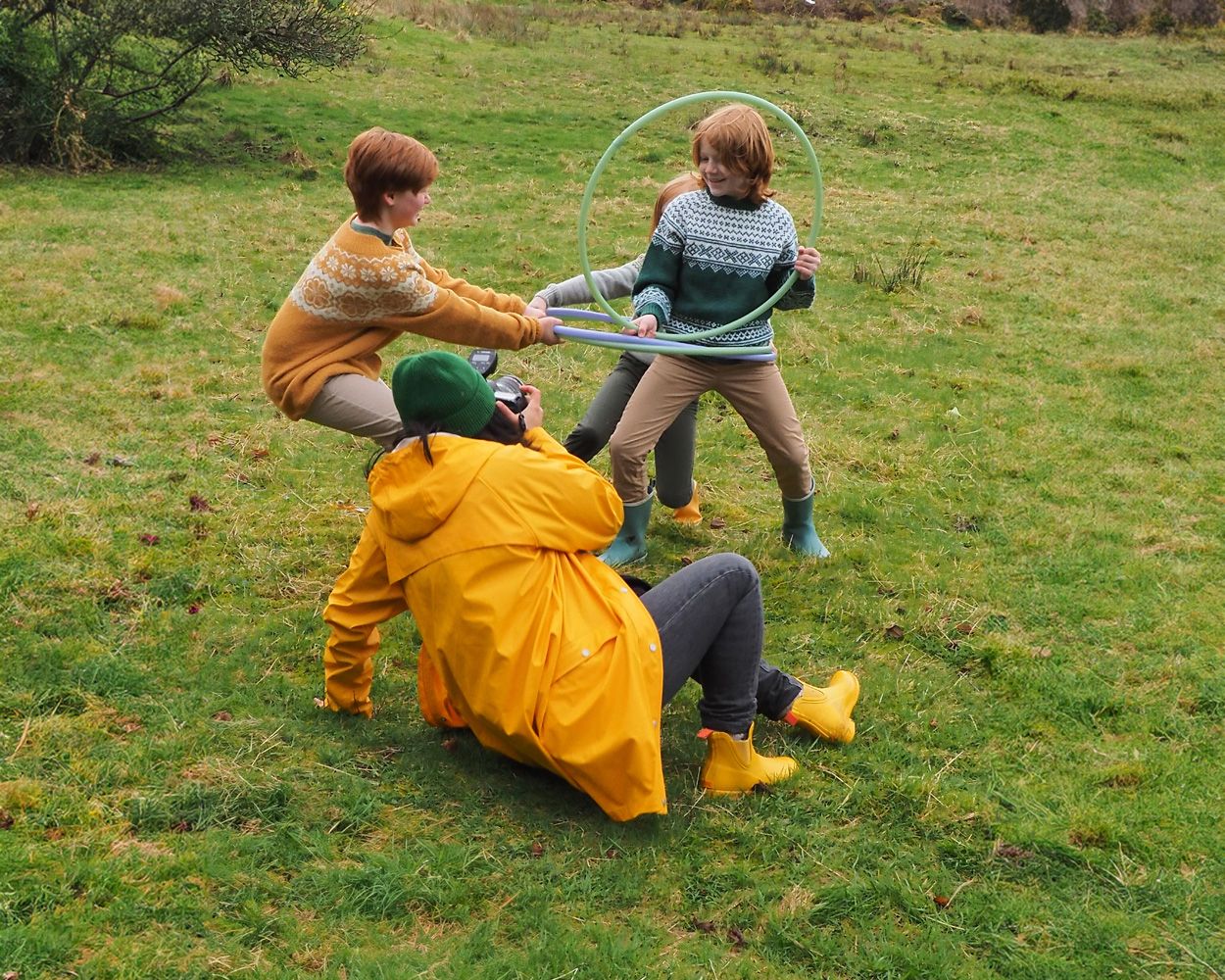 People playing with jump ropes in a grassy field wearing colorful rain gear.