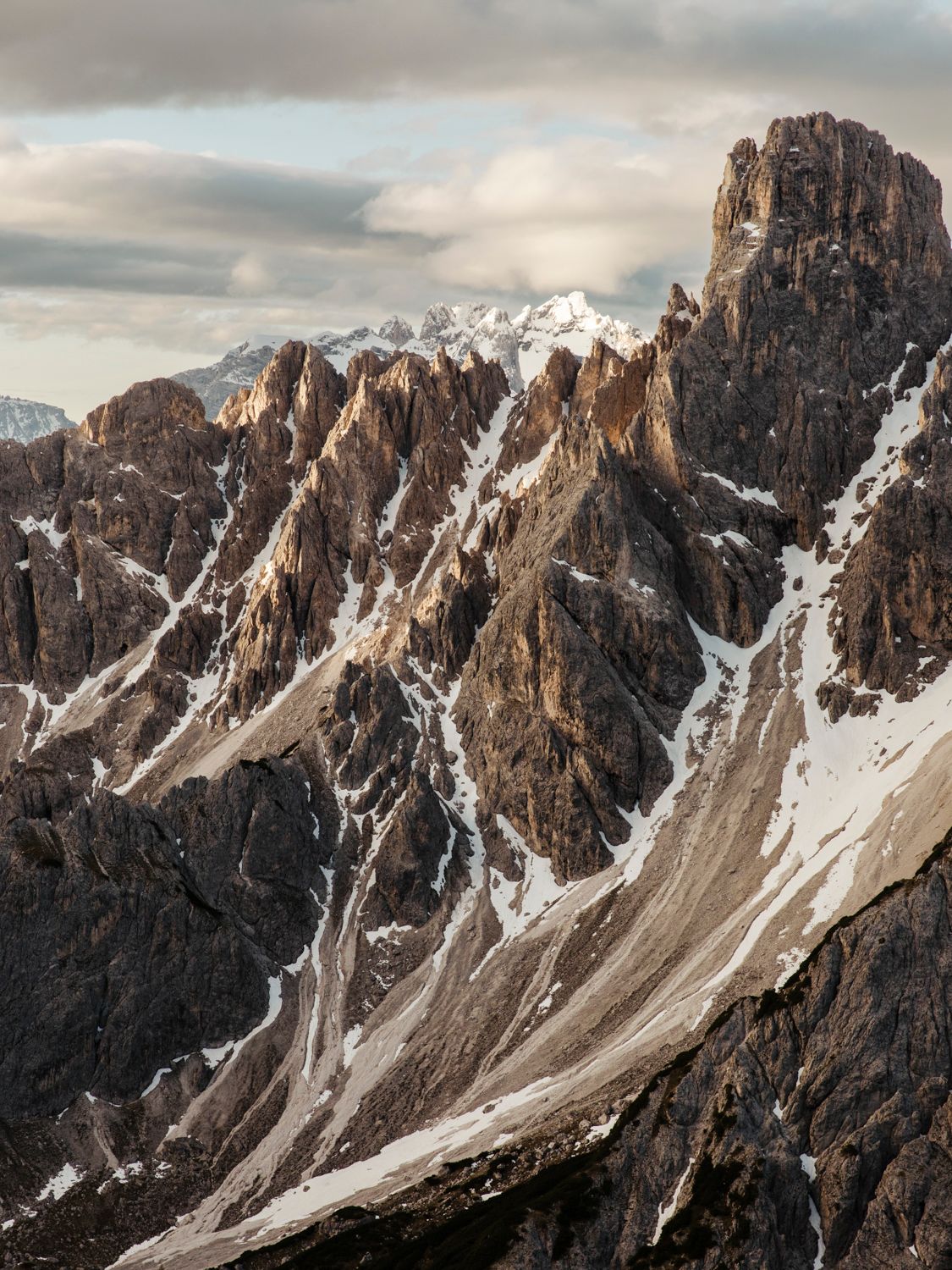 Dramatic rocky mountain peaks with snow patches and warm sunset lighting in the Dolomites.