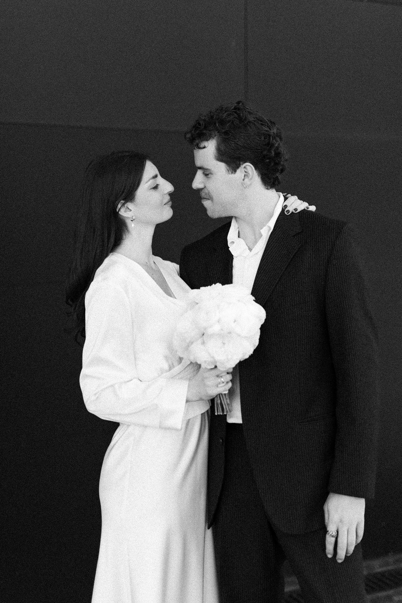 Artistic black and white wedding portrait with couple in intimate pose holding white flowers.