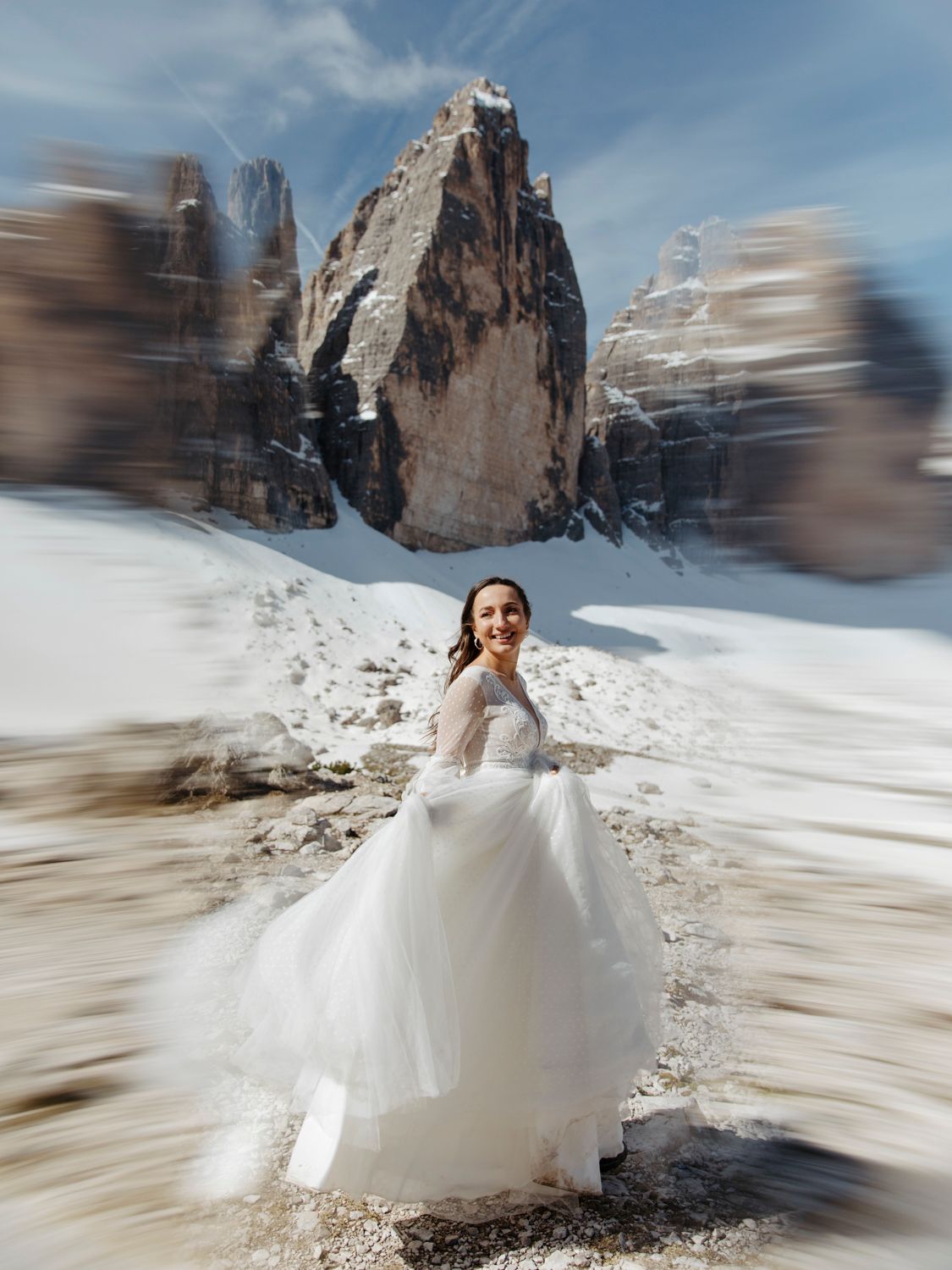 Wedding dress flowing in the wind against dramatic mountain backdrop.
