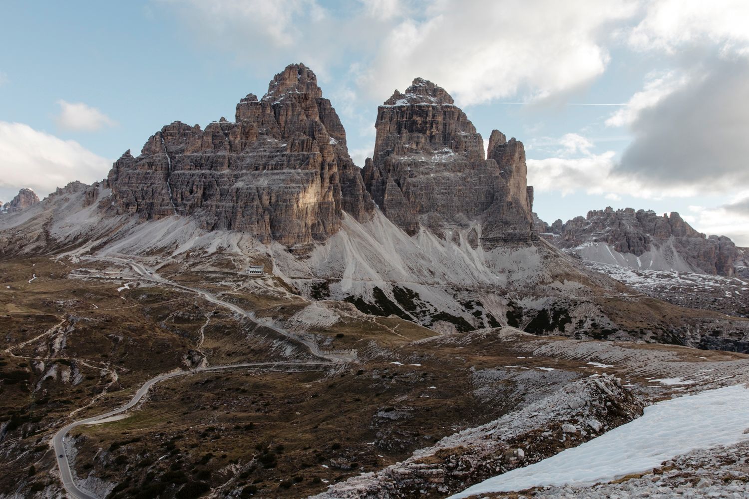Dramatic rocky mountain peaks in the Dolomites with snow patches and rugged cliffs against a cloudy sky.