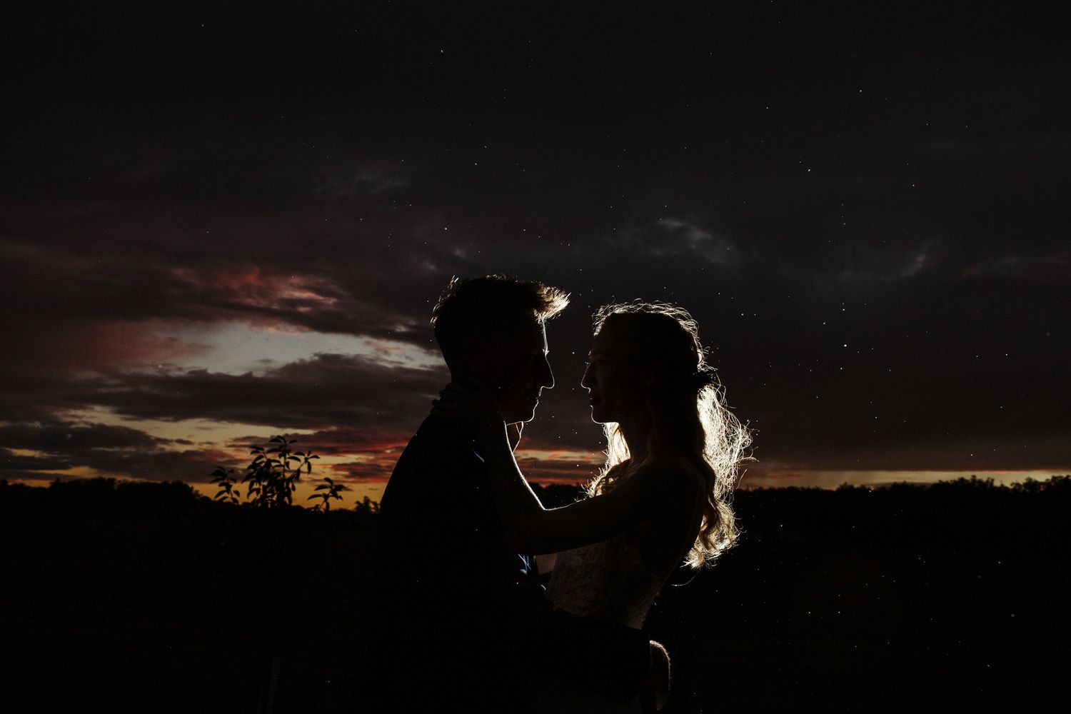 Silhouettes against dramatic sunset sky during outdoor celebration.