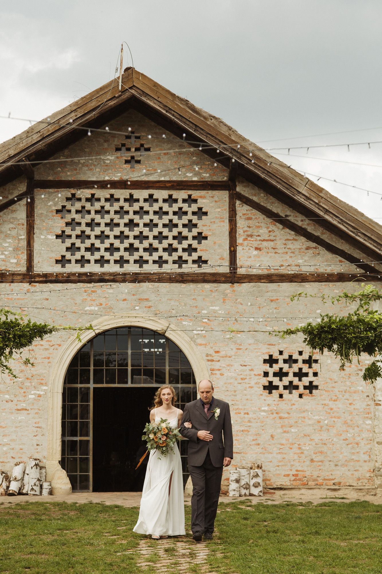 Wedding ceremony in front of a rustic brick building with distinctive cross-pattern architectural details.