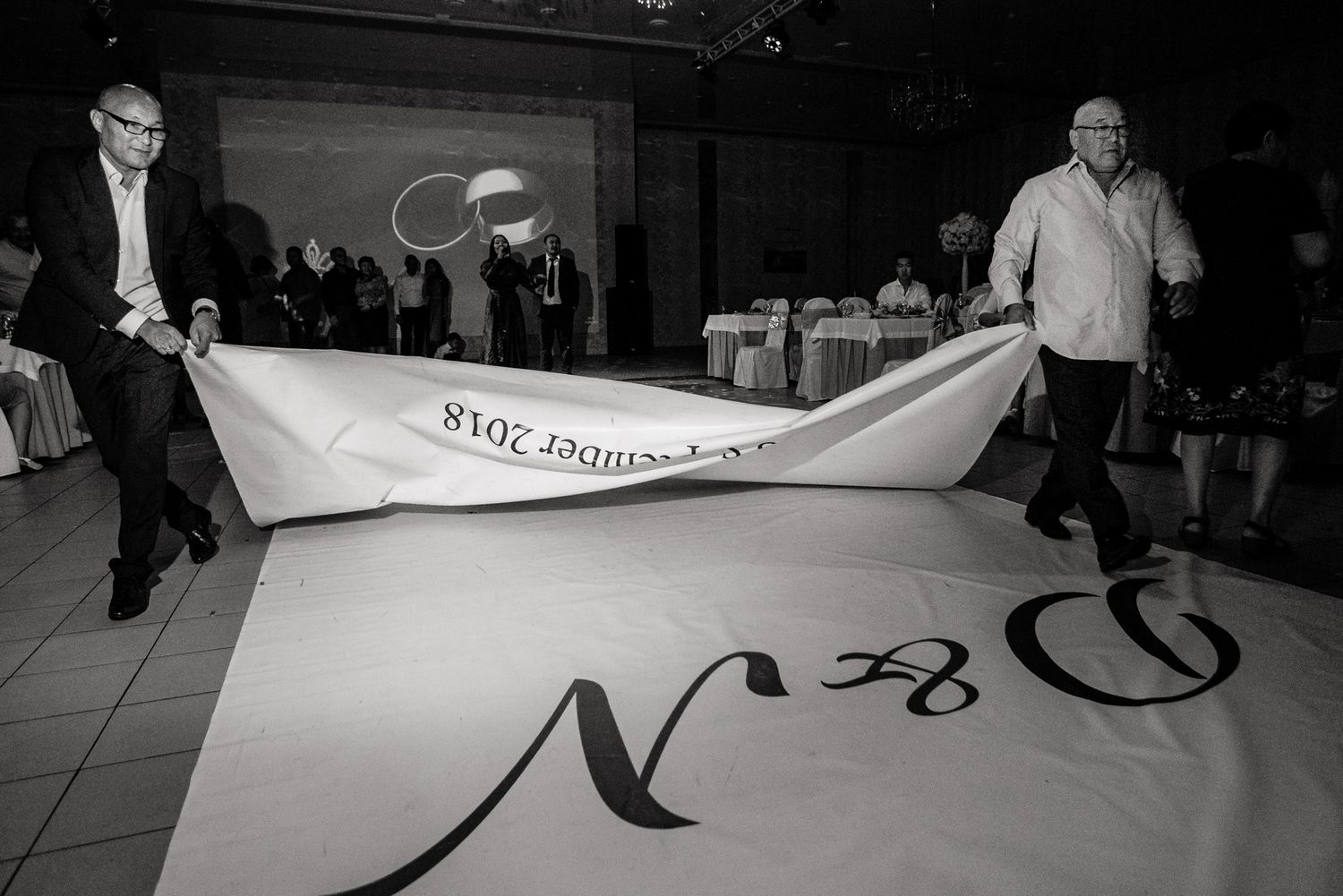 Two men unfurling a large monogrammed dance floor at an event venue.
