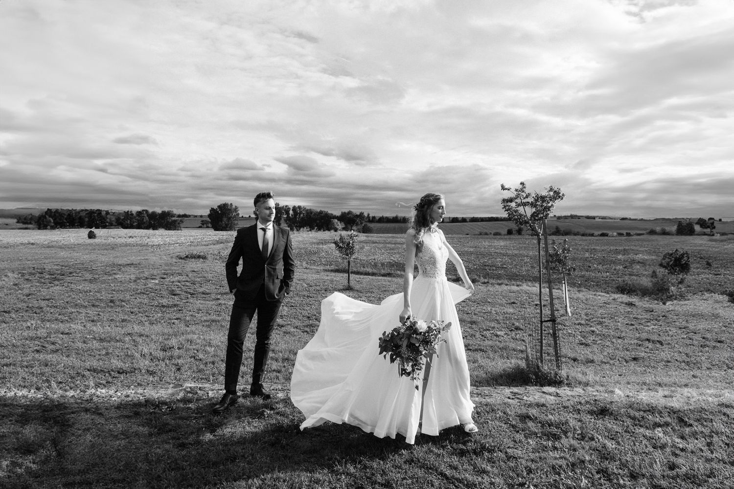 Black and white wedding photo of a couple in an open field with dramatic clouds.