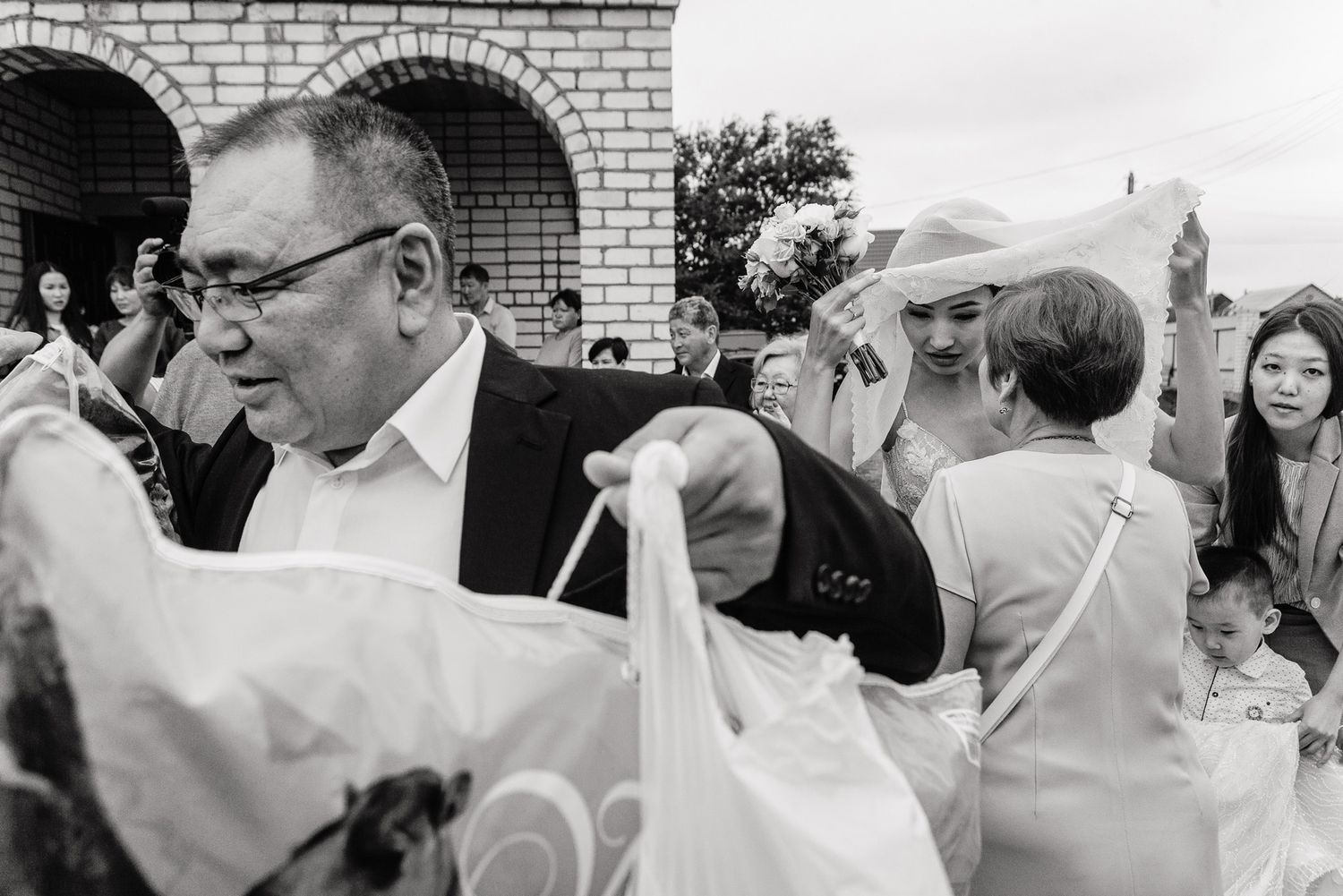 Wedding guests gather outside a brick building with arched doorways during a celebratory moment.