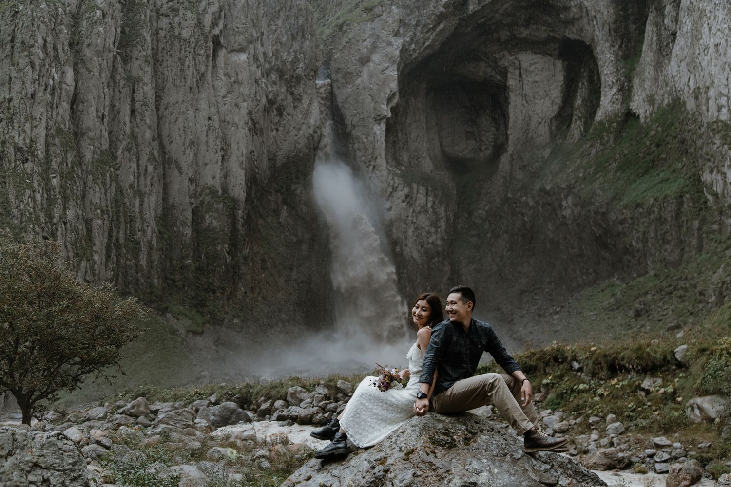 Moody portrait against dramatic waterfall and rocky cliff backdrop.