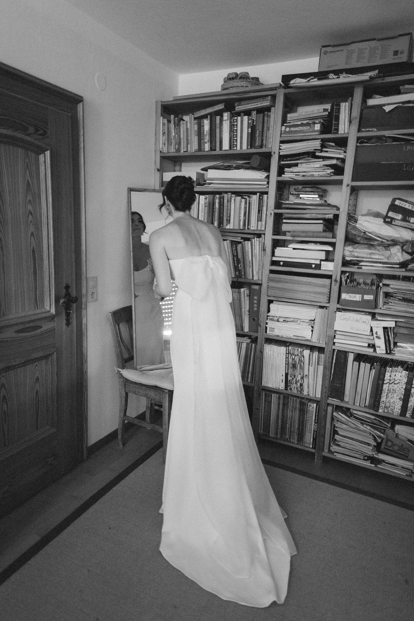 Person in white dress walking through room with floor-to-ceiling bookshelves.