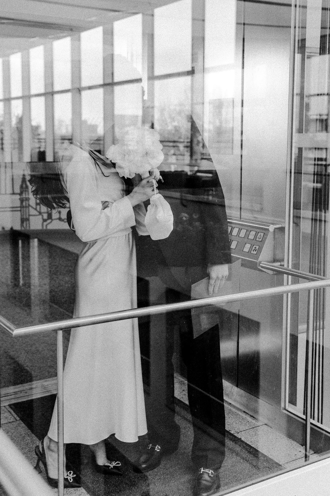 A vintage black and white photograph of a romantic embrace in a light-filled hallway with large windows.