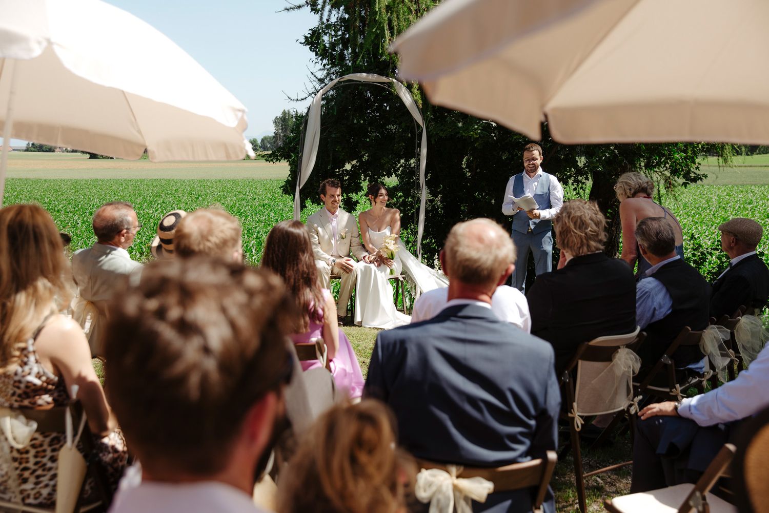 Outdoor wedding ceremony with guests seated under white umbrellas.