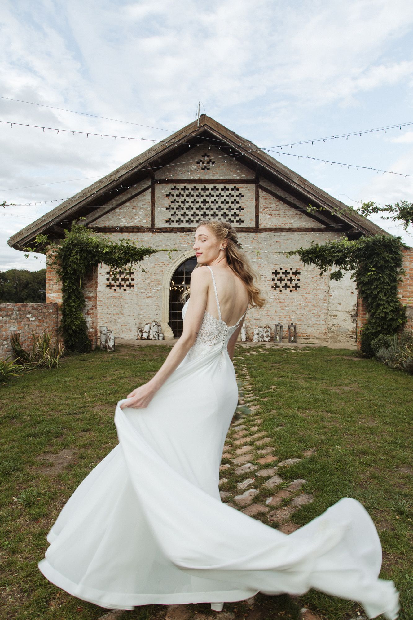 An elegant bridal portrait showing the flowing train of a white dress against a stone barn backdrop.