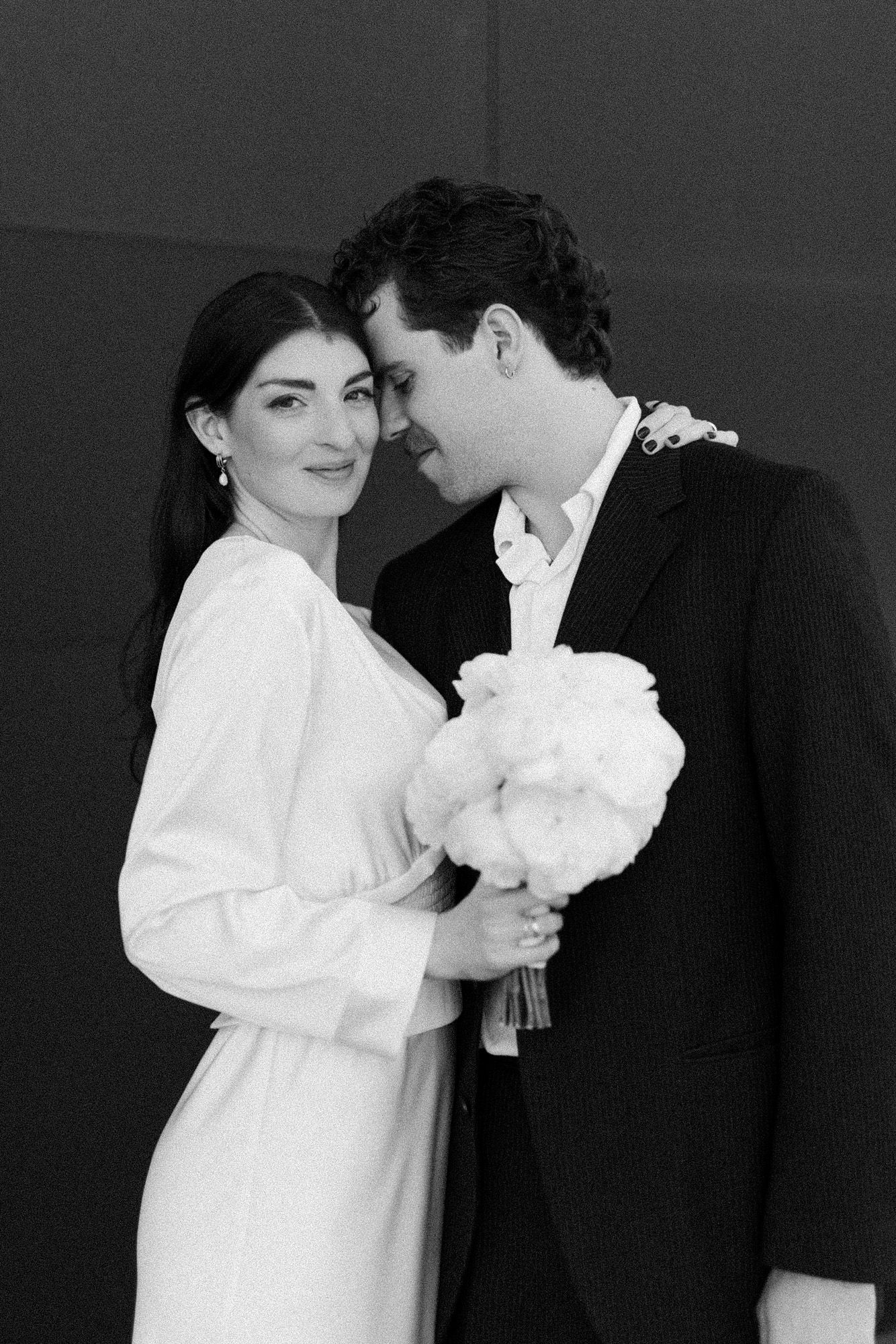 Intimate black and white portrait of couple sharing tender moment with white flowers.