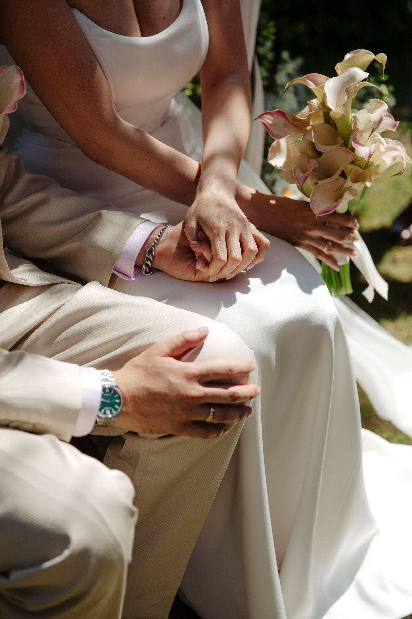 Close-up view of elegant hands holding flowers during an outdoor summer wedding ceremony.