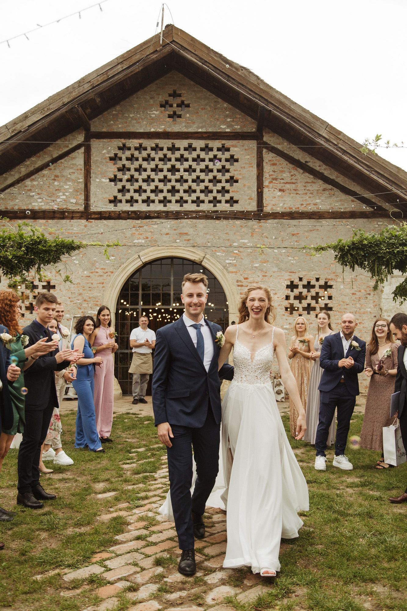Wedding celebration outside rustic brick venue with decorative lattice details and string lights.