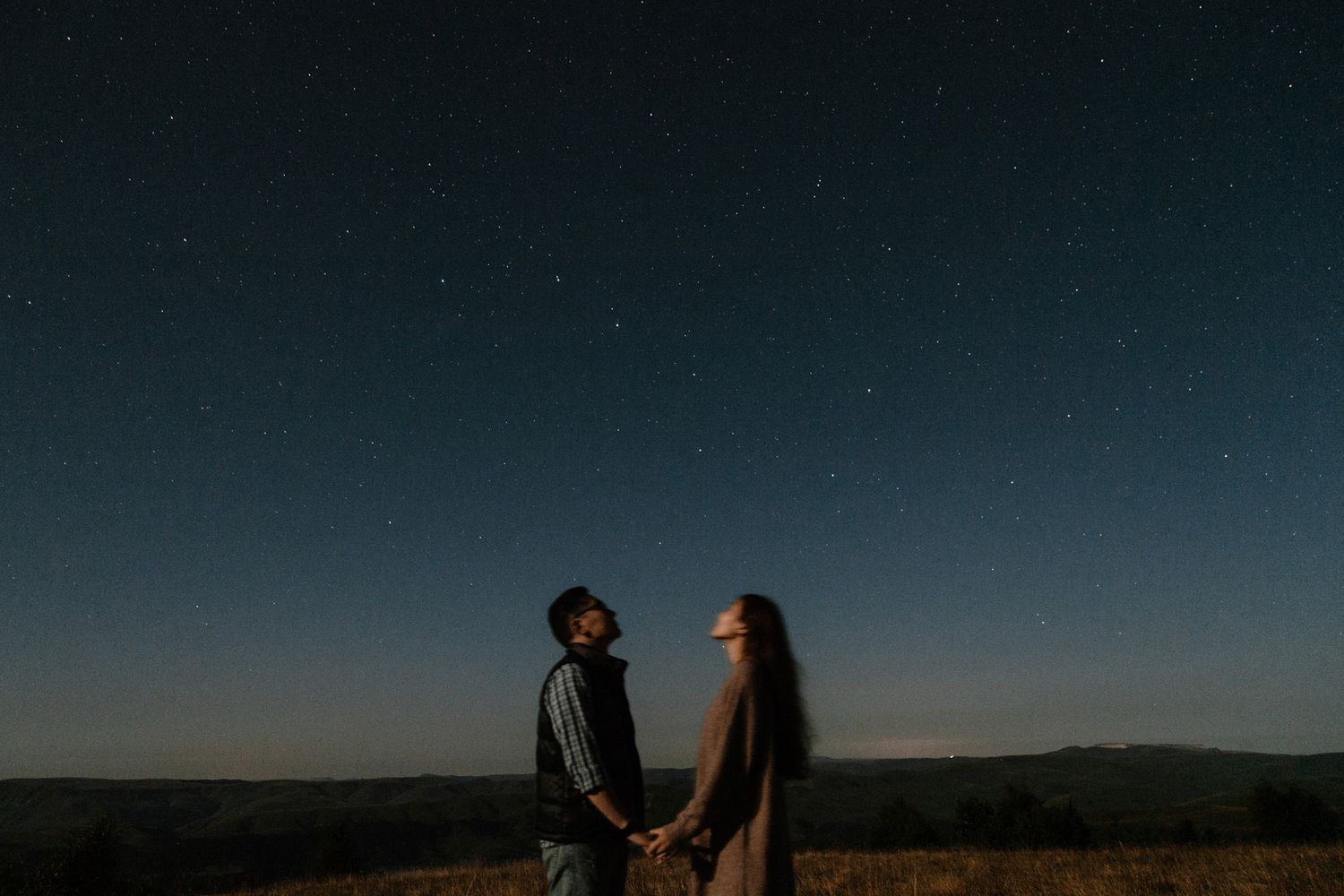 Silhouetted figures holding hands under starry night sky.