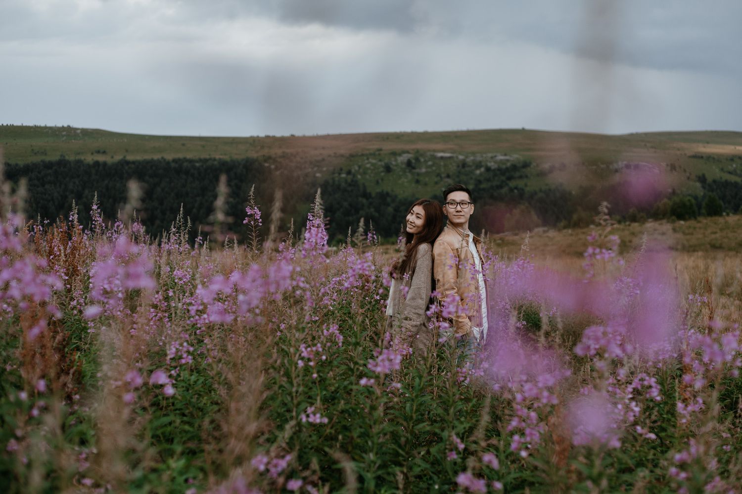 Two people standing among purple wildflowers in a mountain field.
