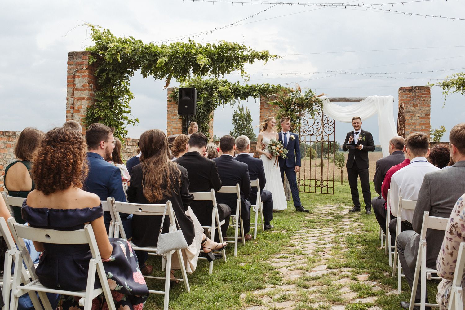 White chairs lined up on grass for outdoor wedding ceremony with brick building in background.