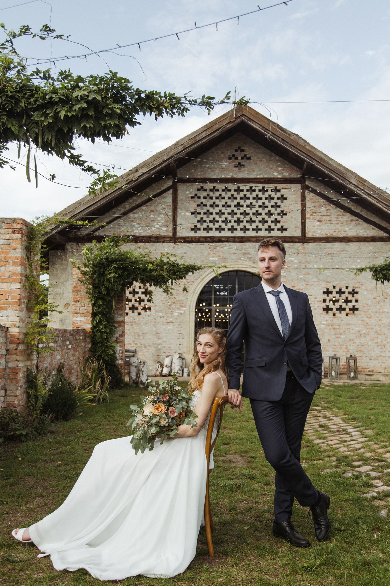 Stylish wedding couple poses against a rustic brick building with decorative lattice details.