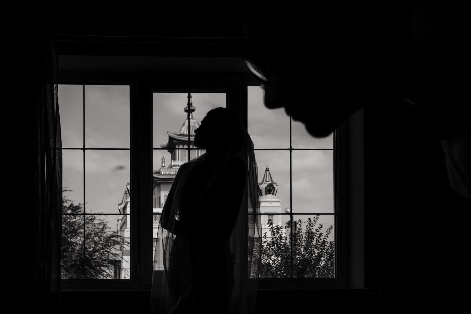 Silhouette stands by window with tower visible in distance.