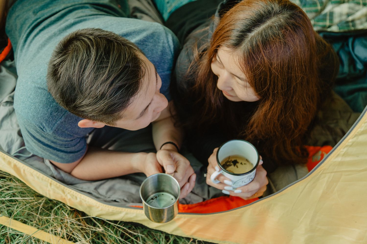 Close-up view of couple lying down together sharing warm drinks outdoors.