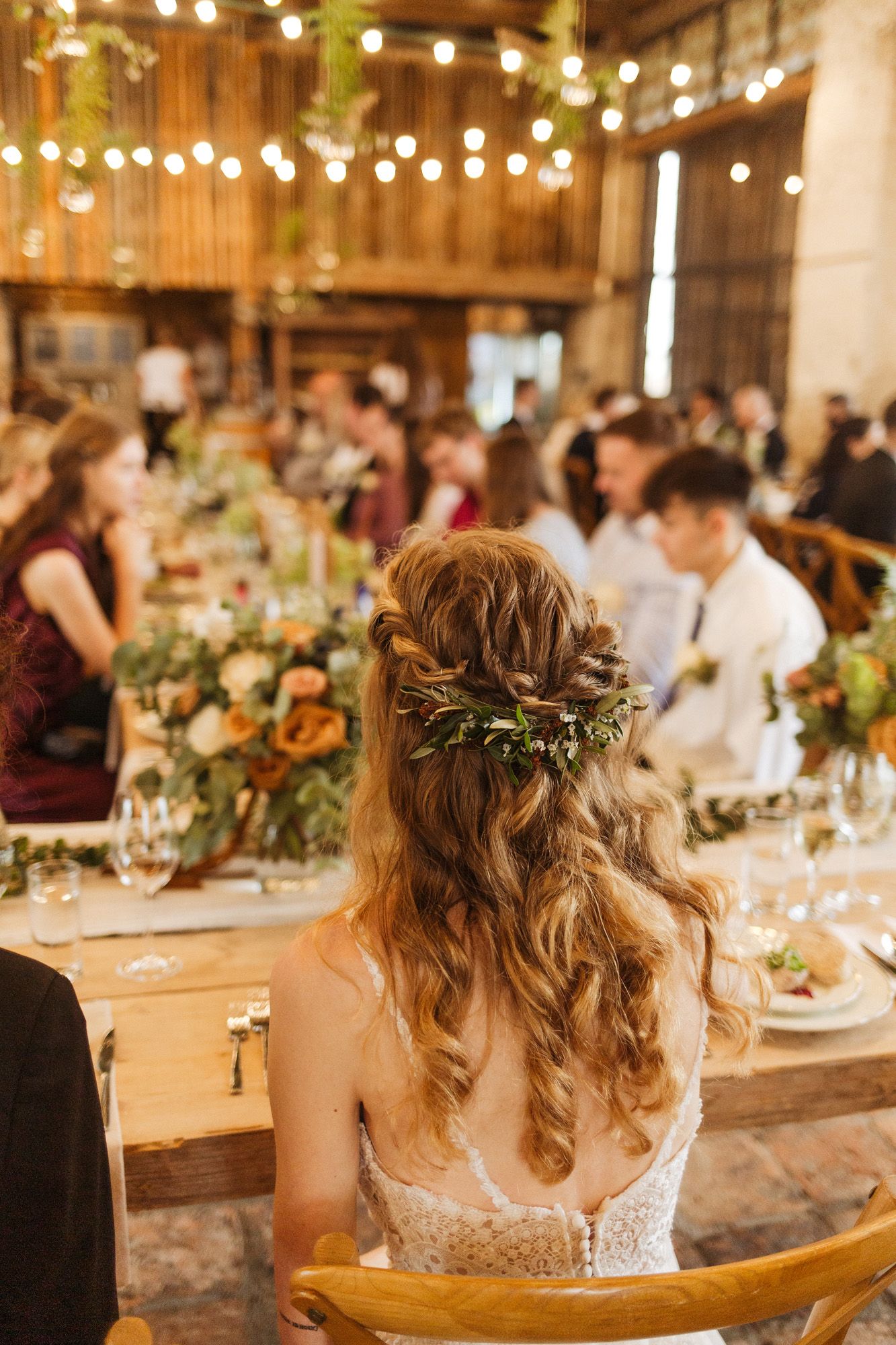 Wedding reception table setting with floral arrangements and string lights in rustic barn venue.