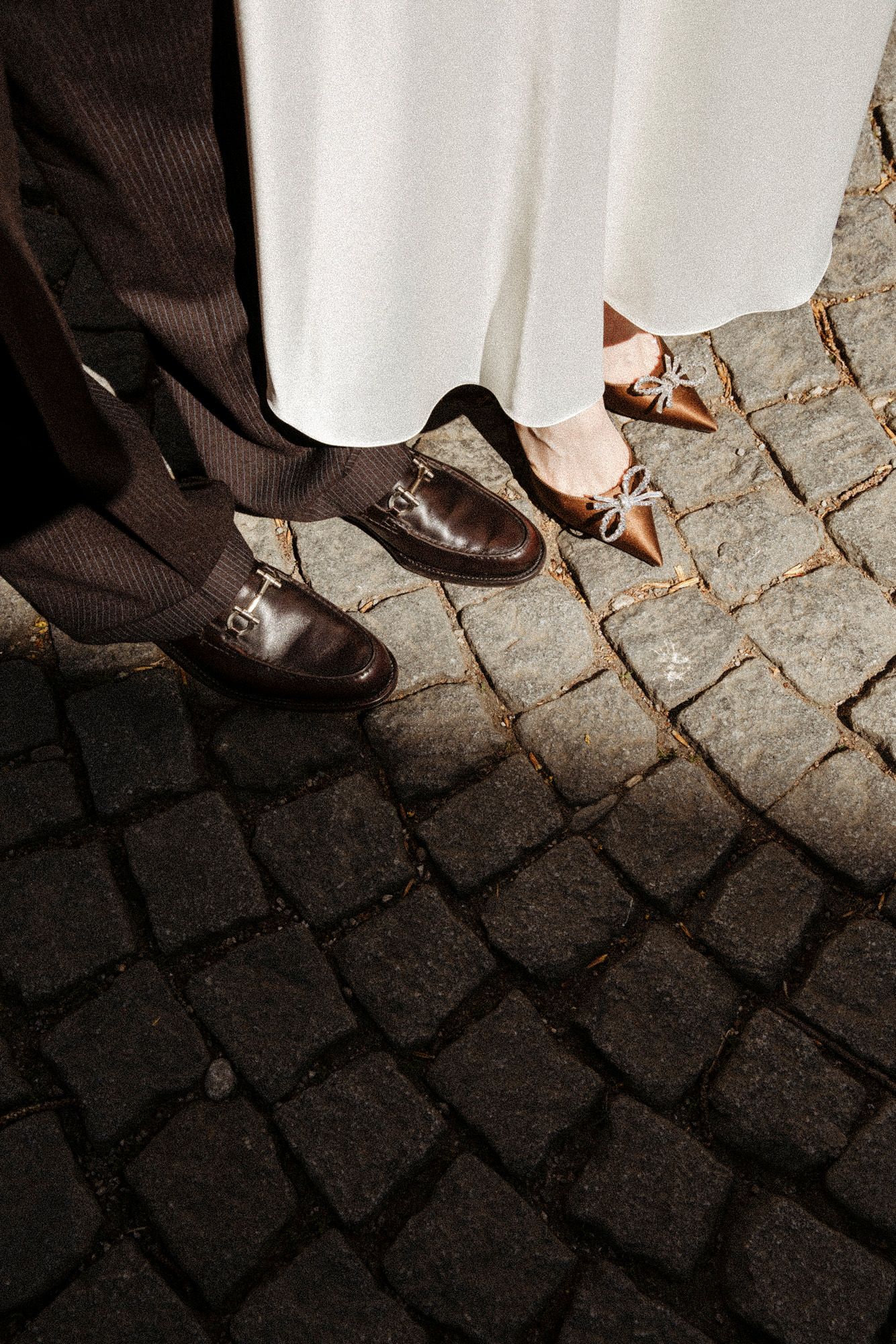Close-up of bride and groom's feet on cobblestone, showing brown dress shoes and nude heels.