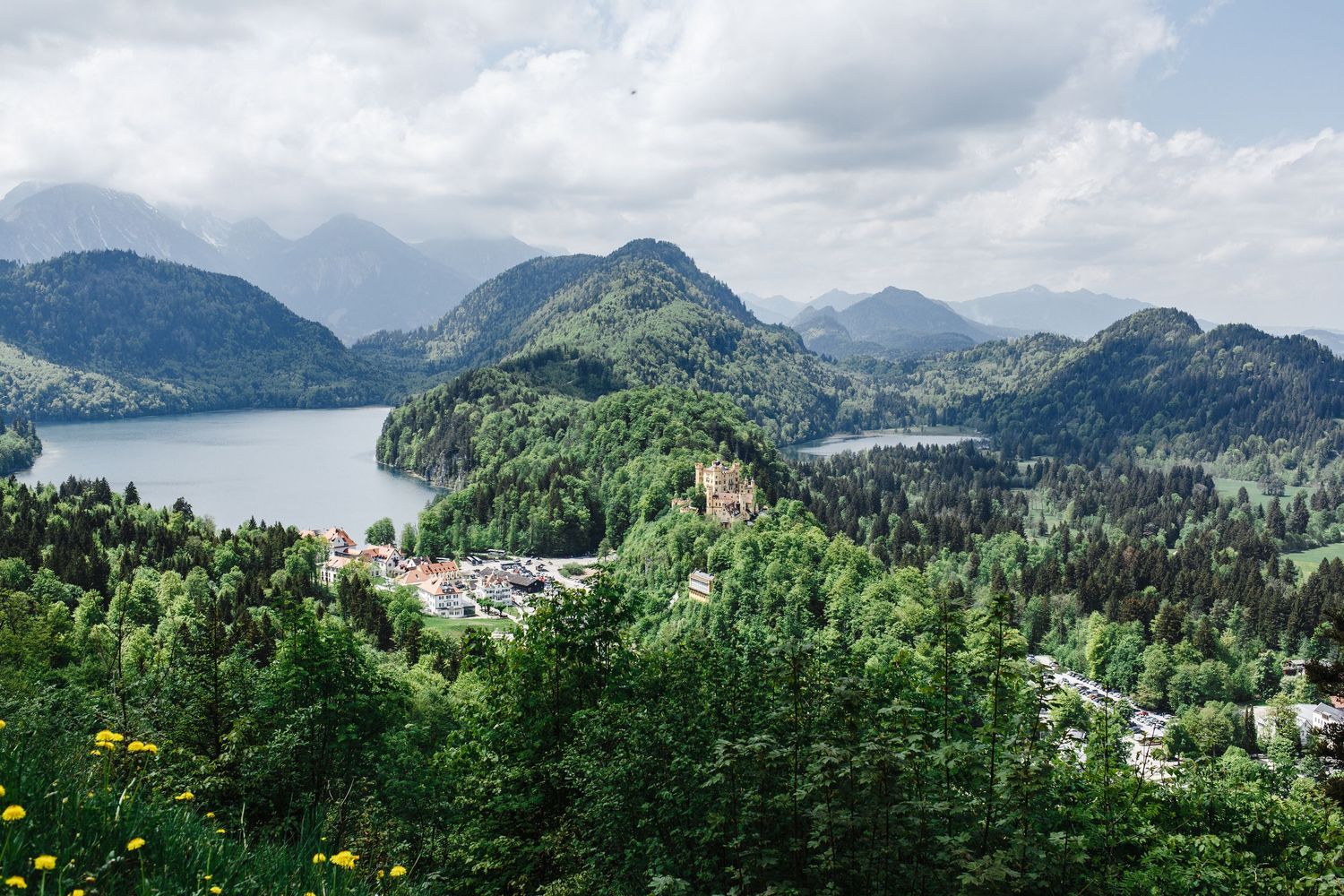 Panoramic view of mountain lake surrounded by lush green forests and distant peaks.