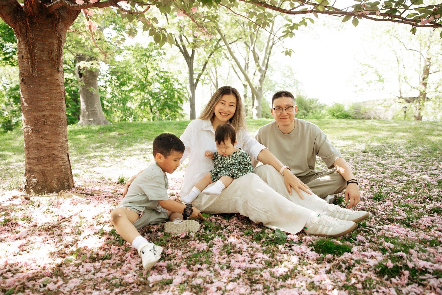 Family relaxing together on grass under blooming trees in a garden setting.