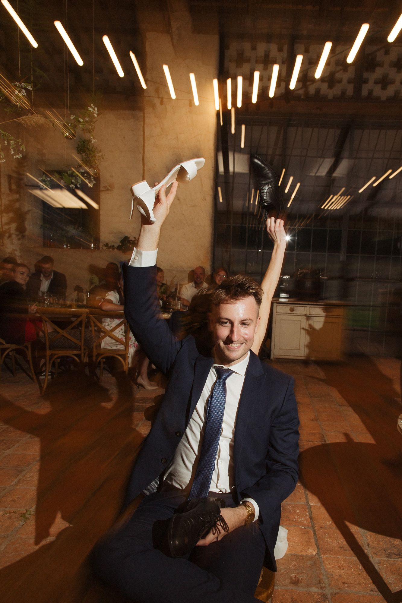 Person celebrates at indoor event venue with raised arms under dramatic lighting.