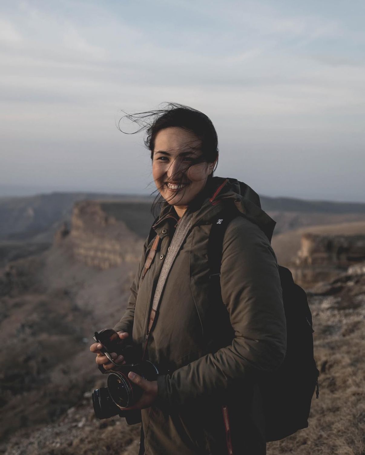 Adventure photographer with camera gear poses against desert canyon backdrop.