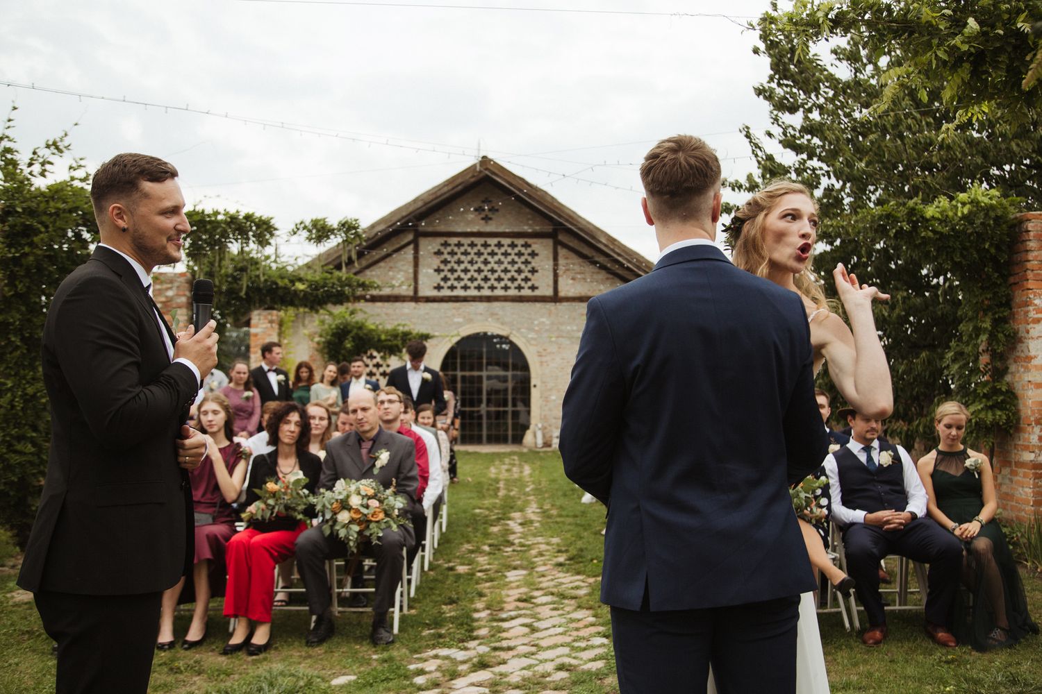 Guests celebrating at an outdoor wedding ceremony with a historic brick building backdrop.