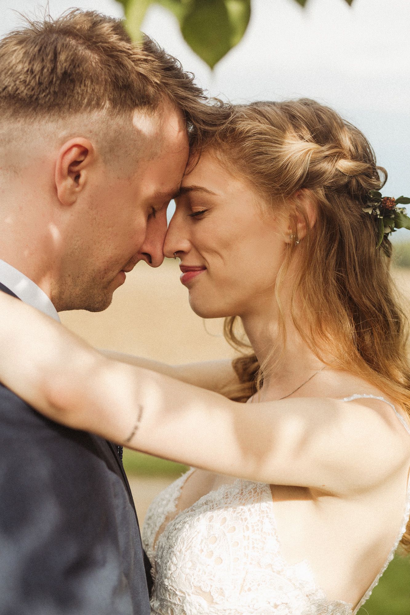 A tender forehead-touching moment between newlyweds in an outdoor garden setting.