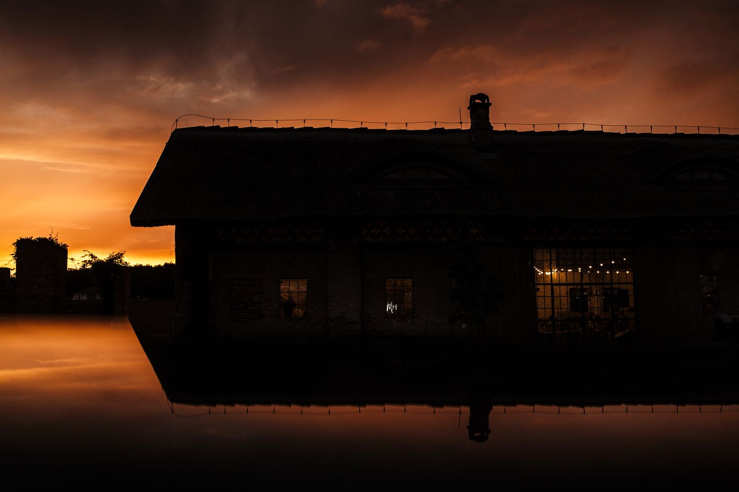 Silhouette of a house against dramatic orange sunset with water reflection.