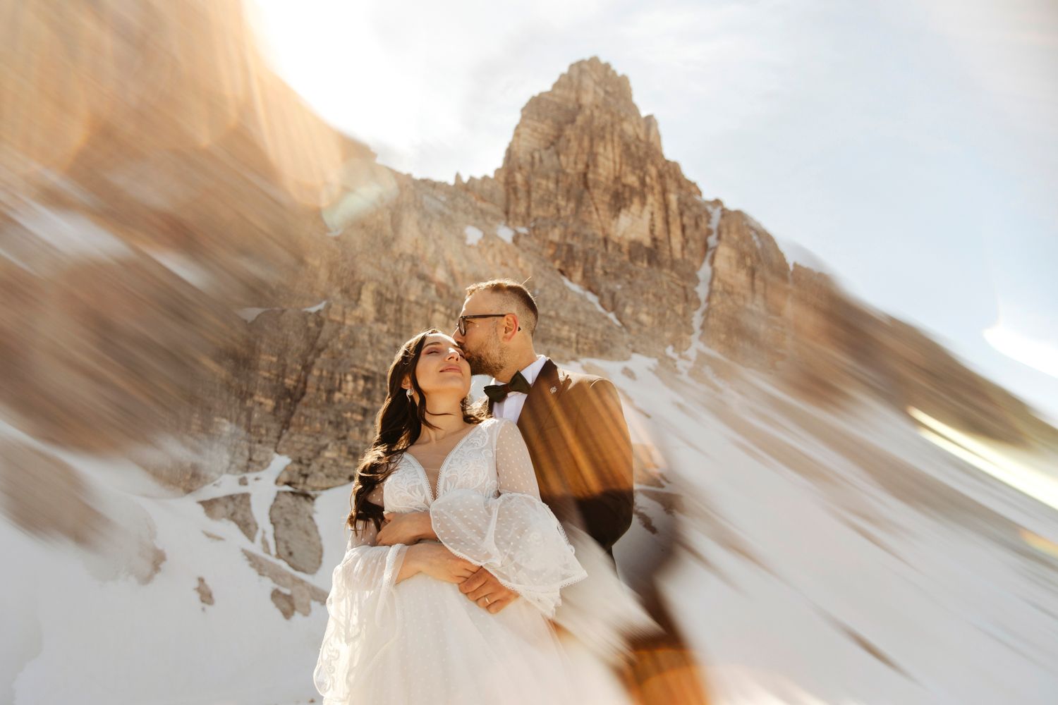 Couple sharing an intimate moment in front of snowy mountain peaks.