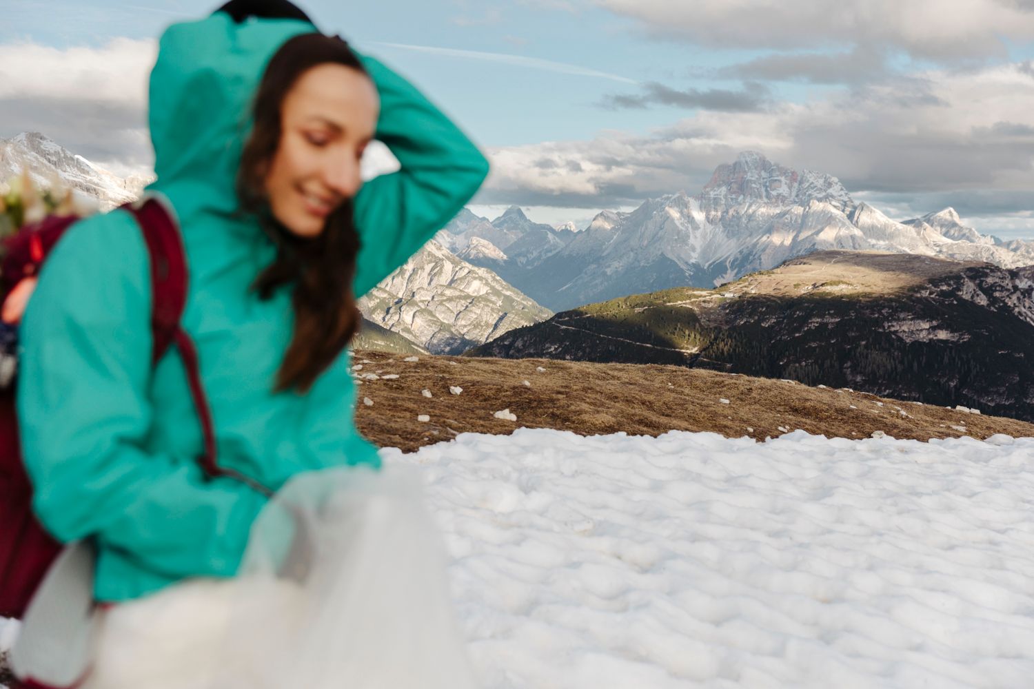 Adventure bride in teal hoodie enjoying snowy mountain views during winter elopement.