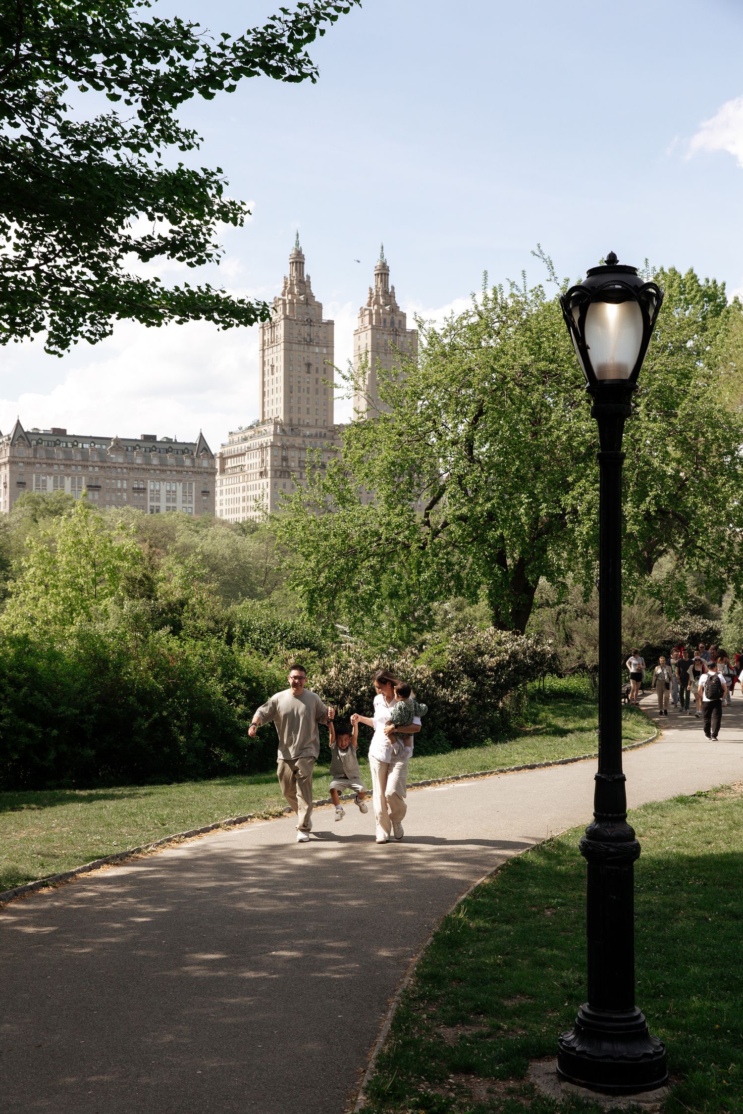 Couple walking along path in Central Park with historic architecture in background.