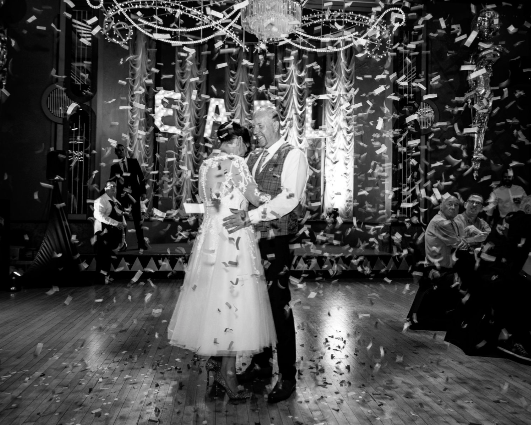 Romantic couple dancing amid falling confetti in black and white.