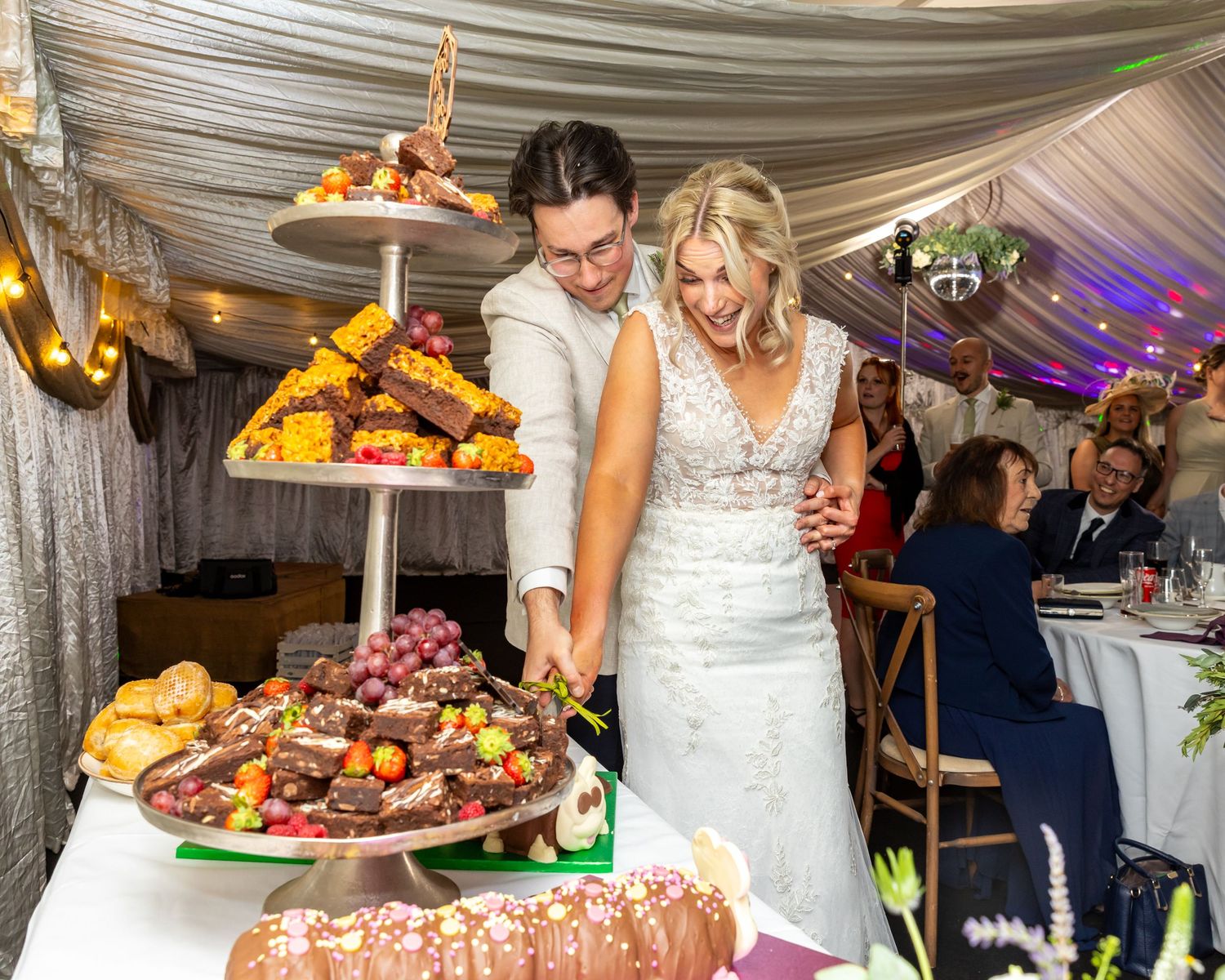 Wedding reception buffet table with assorted desserts and appetizers under white tent.
