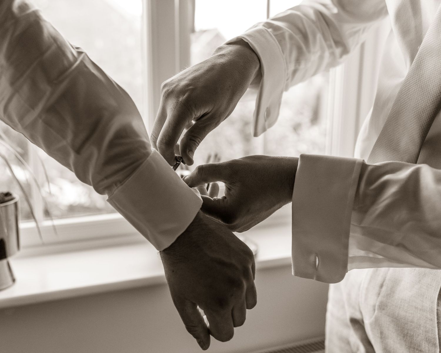 Black and white image of hands adjusting formal wear cuffs near window.