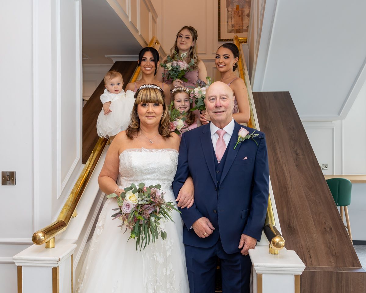 A wedding party stands on an elegant staircase with brass railings during a celebration.
