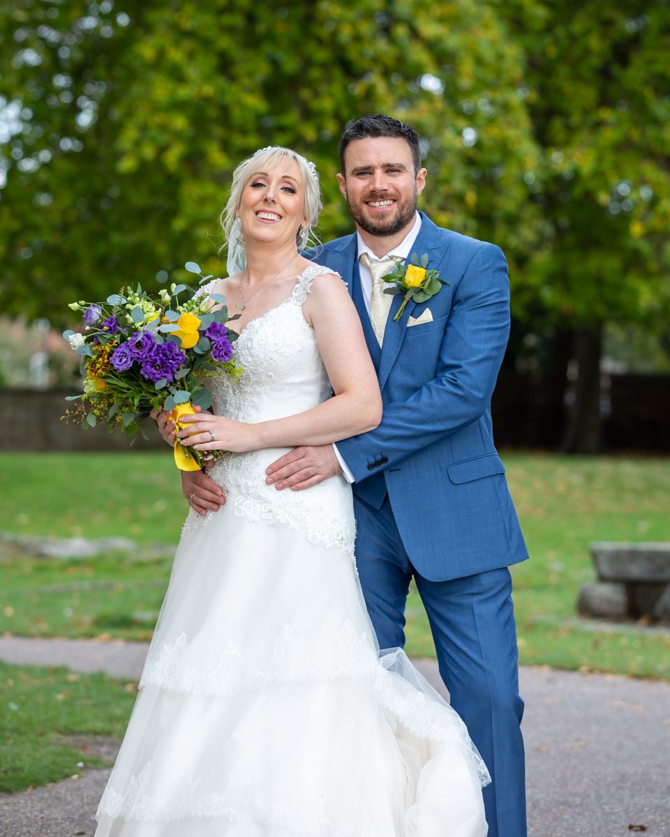 Couple in wedding attire posing together on garden pathway.