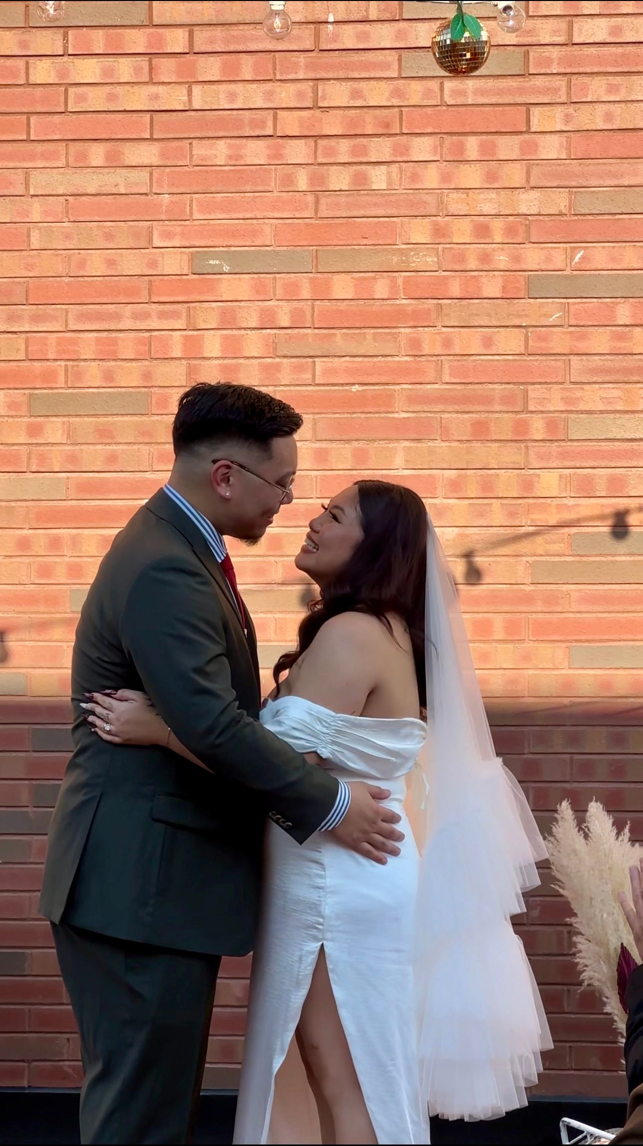 Couple embracing in formal attire against a brick wall background.