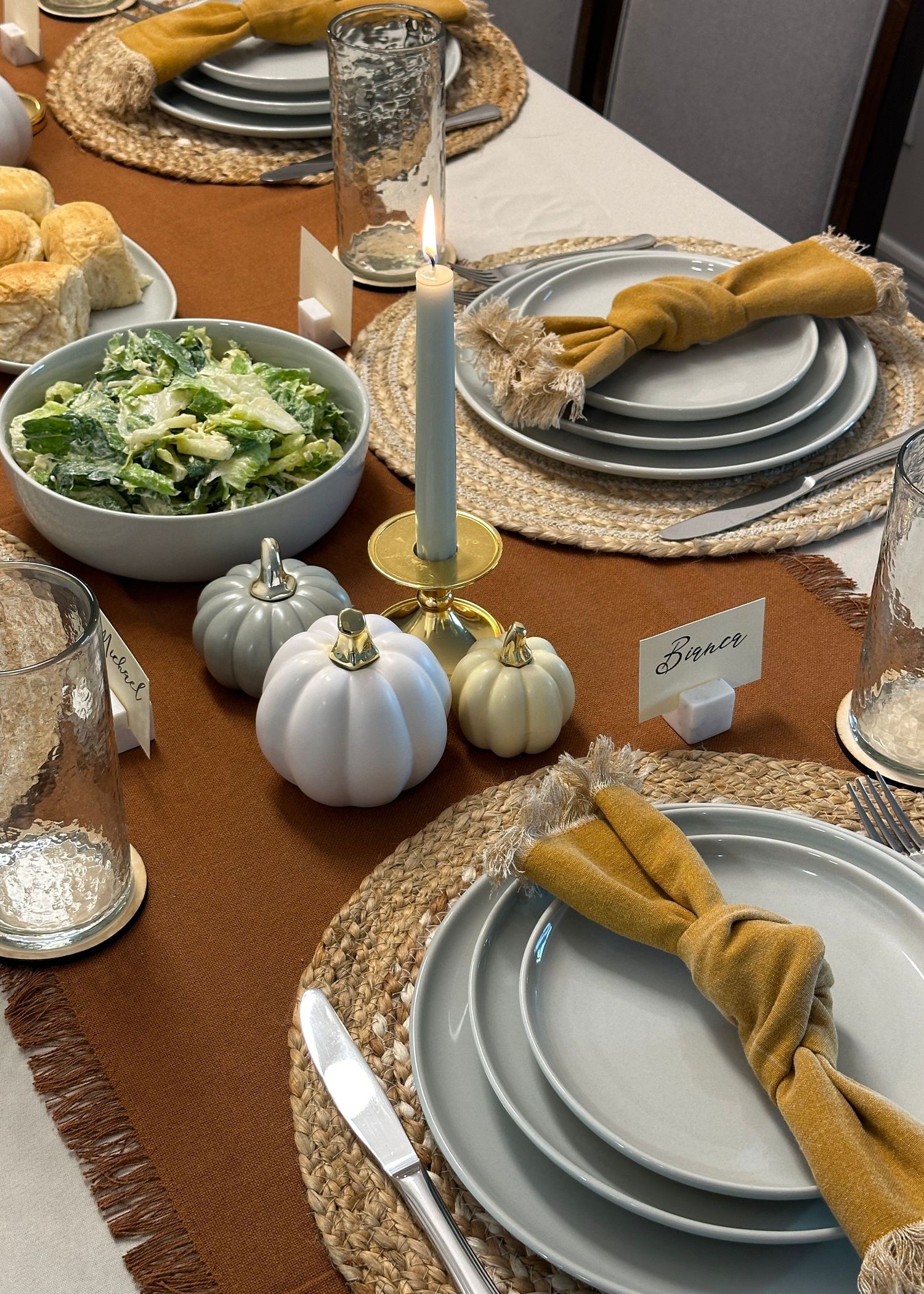 Autumn table setting with gray plates, gold napkins, and white decorative pumpkins.