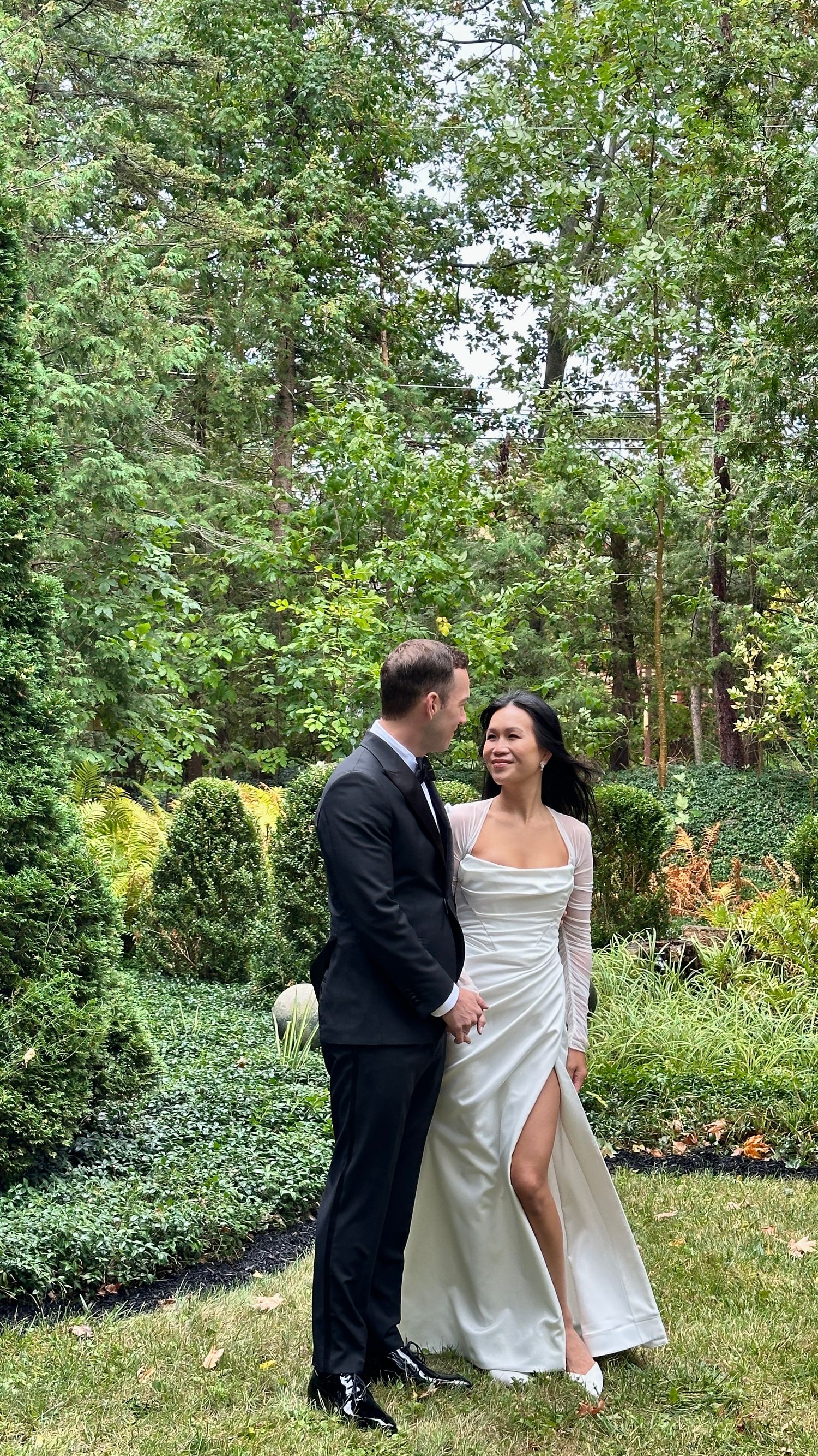 Couple in wedding attire sharing a joyful moment in a lush garden setting.