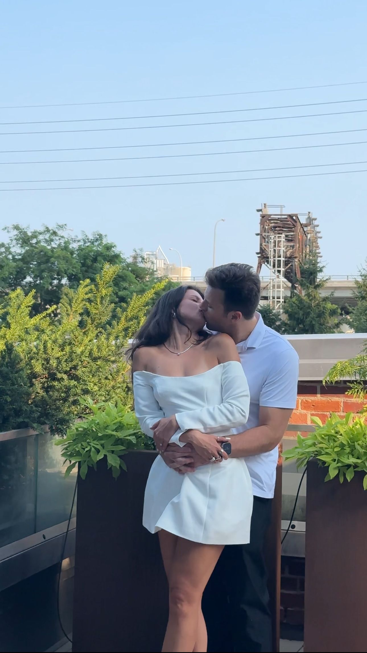 Romantic rooftop moment between couple with city skyline and power lines visible.