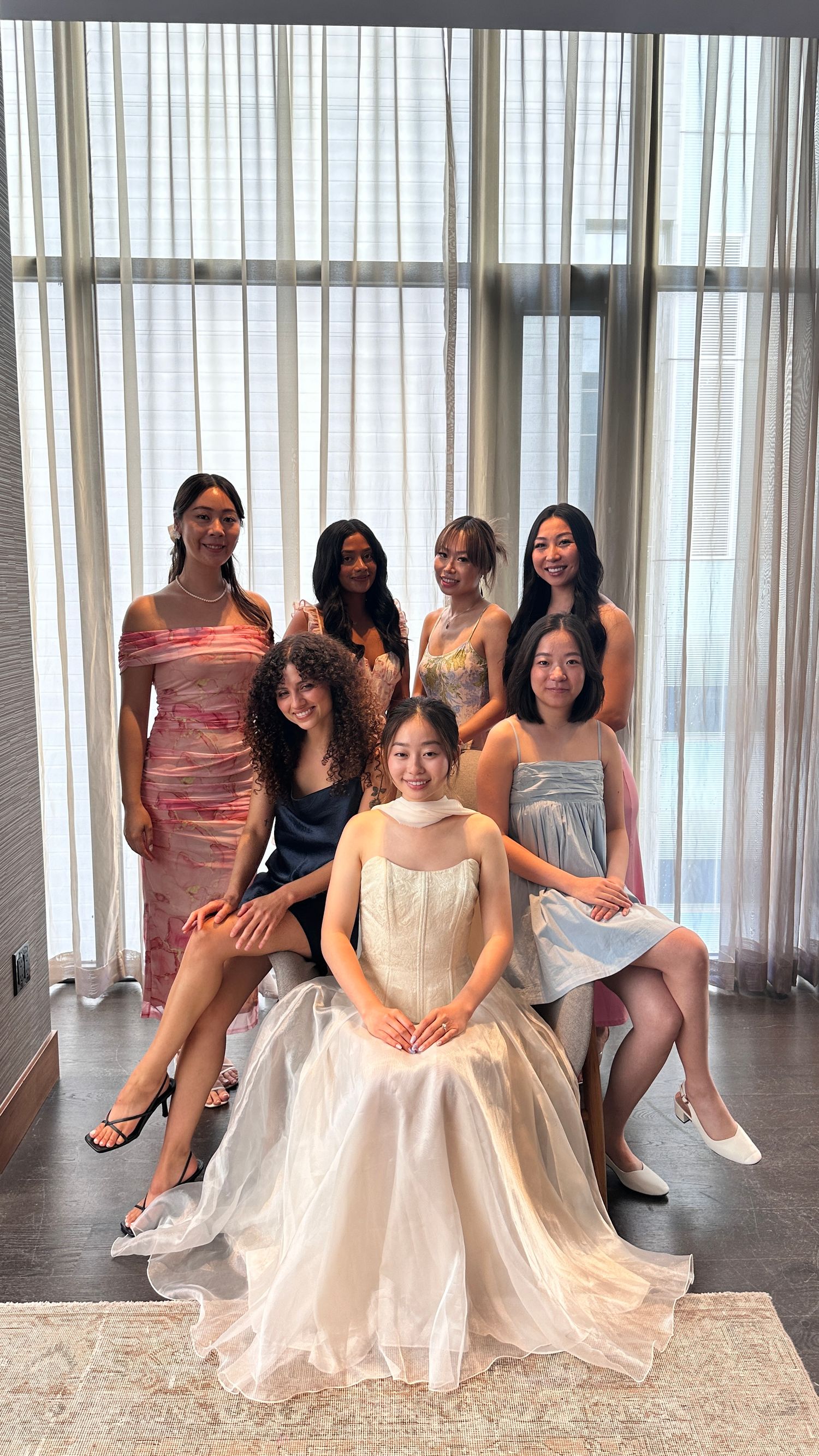 Bridal party poses together in formal dresses with bride seated center in white gown.